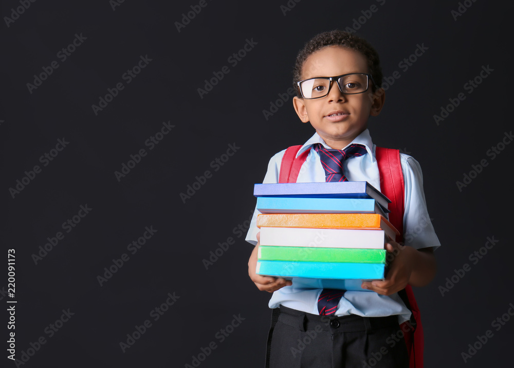 Funny African-American schoolboy with books on dark background