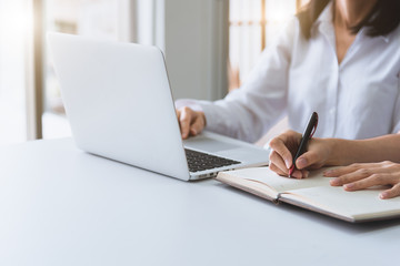 Close up of two businesswoman using laptop and writing on notebook in the morning. Business and financial concept. People and lifestyles concept. Office and workplace theme.