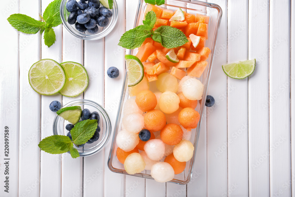 Plate with delicious melon balls and berries on white wooden table