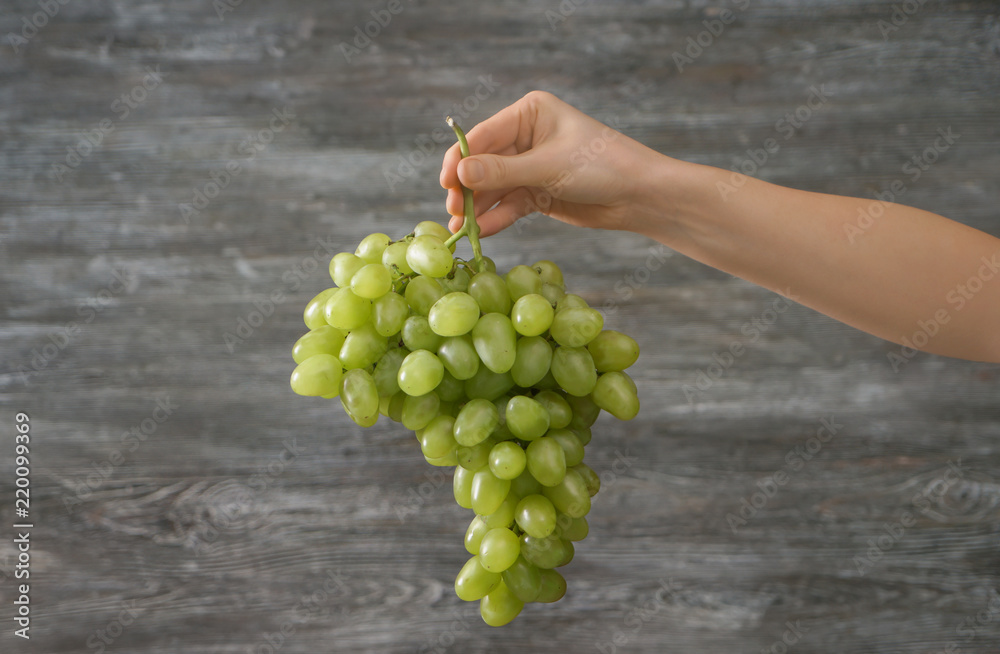Woman holding ripe grapes on grey background