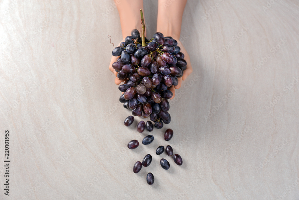 Woman holding fresh ripe grapes on light background
