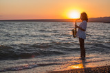 Fototapeta  - Silhouette of young sexy woman playing saxophone on the beach at sunset