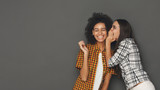 Fototapeta  - Young woman whispering to her friend against grey background
