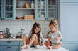 © teksomolika - Two little girls in the kitchen sitting on the table.