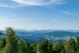 Fototapeta Na ścianę - View from top of a mountain in the valley with clouds on the sky and mountains on the background and trees in front of in the bavarian forest