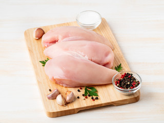 raw chicken breast fillet with spices on a wooden board on white wooden table, side view