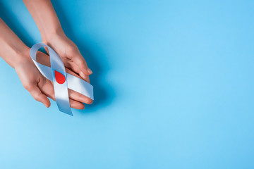 the blue ribbon awareness with red blood drop in woman hands isolated on a blue background. World diabetes day,14 november. Copy space. Top view