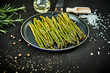 delicious green asparagus in a pan on a wooden black table with rosemary salt and olive oil