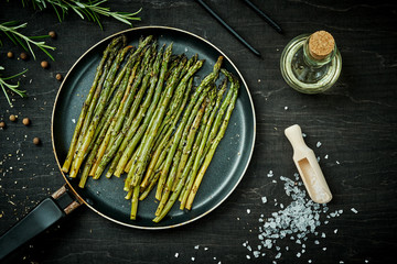 delicious green asparagus in a pan on a wooden black table with rosemary salt and olive oil