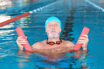 Wall Mural - Sportive senior man with swimming noodle in indoor pool