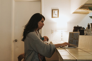 Mother using a computer and holding her baby