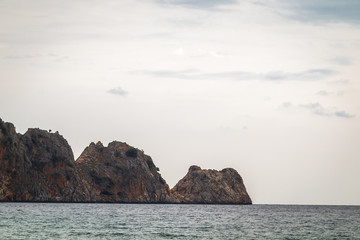 row of brown big rocks in the calm waving sea. cloudy weather in a summer day. view from the beach of the hotel