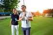 © zorandim75 - Portrait of smiling couple holding golf clubs while standing on field