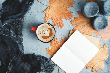 Wall Mural - Autumn flat lay composition on a grey concrete background. Maple leaves, the open notebook with empty sheets, cocoa, black aromatic candles and warm scarf. Mockup, top view.