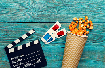 Clapperboard, glasses and popcorn on blue wooden background top view with copyspace