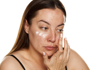 beautiful middle-aged woman applying moisturizer on her face on white background