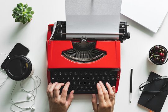 Top view of woman hand working with bright red vintage typewriter
