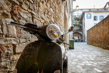 Typical Street Scene In Italy With A Black Scooter Or Moped On An Old Narrow Cobblestoned Street. Travel Concept