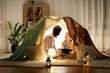 family, hygge and technology concept - happy mother and little daughter with tablet pc computer in kids tent at night at home