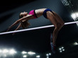 The female athlete in action. high jump over bar at stadium at night