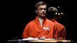 Handcuffed maniac in orange prison jumpsuit looking around in interrogation room
