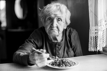 Wall Mural - An elderly woman eats sitting at the table. Black and white photo.