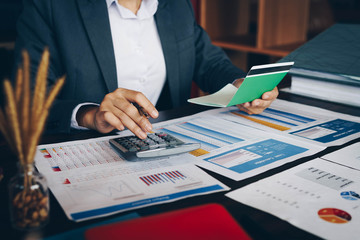 Businesswoman on desk in office using calculator to calculate saving account passbook and statement with financial report .Female accountant or banker use calculator. Savings, finances and economy con