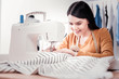 Talented woman. Cheerful young dressmaker being concentrated while using sewing machine for creating stylish clothes