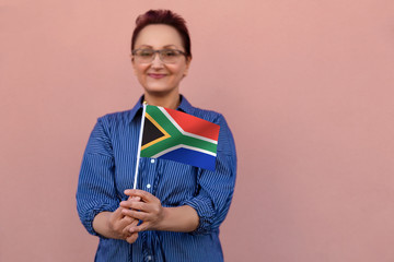 Wall Mural - South Africa flag. Woman holding South Africa flag. Nice portrait of middle aged lady 40 50 years old with a national flag over pink wall background outdoors.