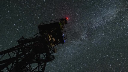 milky way galaxy circling over communication tower in starry night sky time lapse zoom