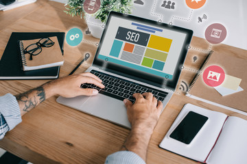 cropped shot of developer using laptop with SEO icons at workplace