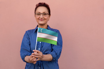 Wall Mural - Uzbekistan flag. Woman holding Uzbekistan flag. Nice portrait of middle aged lady 40 50 years old with a national flag over pink wall background outdoors.