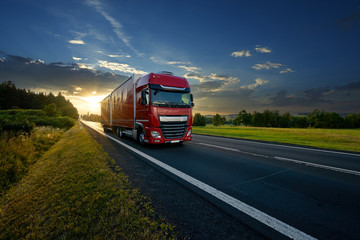 Wall Mural - red truck arriving on the asphalt road in rural landscape in the rays of the sunset