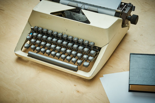 bright old typewriter with gray keys and a book on a wooden table