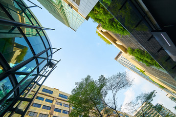 Low angle shot of modern glass buildings and green with clear sky background.