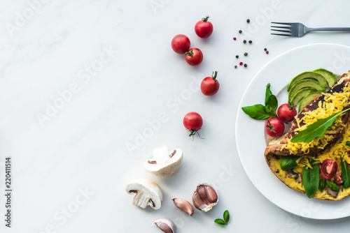 Fotografía top view of homemade omelette with cherry tomatoes, avocado pieces and cutlery o