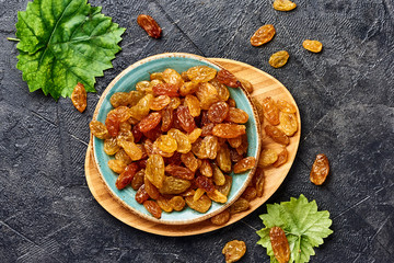 Wall Mural - Yellow big raisins on black concrete background. Top view of dried grapes.