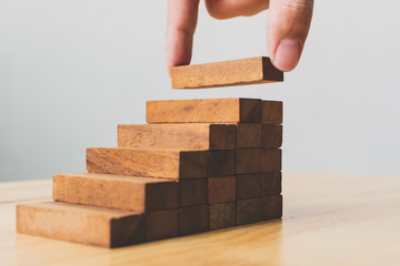 Hand arranging wood block stacking as step stair. Ladder career path concept for business growth success process