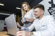 © Maksym - A picture of businessman sitting at table. He is looking at laptop nad holding hand near it. Girl is standing besides man and holds a cup of coffee. She looks at the laptop screen