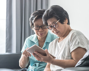 Wall Mural - Aging society concept with Asian elderly senior adult women twin sisters using mobile digital tablet application technology for social media network among friends community via internet communication