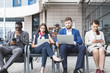 © xartproduction - Group of happy diverse male and female business people team in formal gathered around laptop computer in bright office against the background of a glass building