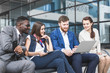 © xartproduction - Group of happy diverse male and female business people team in formal gathered around laptop computer in bright office against the background of a glass building