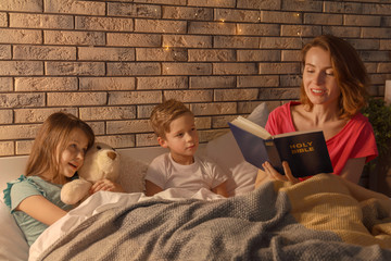 Mother reading Bible to her little children in bed