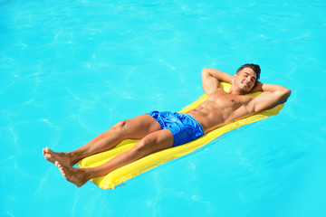 Wall Mural - Young man with inflatable mattress in pool on sunny day