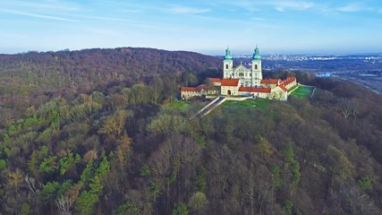 Wall Mural - Camaldolese monastery and baroque church in the wood on the hill in Bielany, Krakow, Poland , Aerial 4K video in sunset light in winter with Vistula River and far view of Cracow city in the background