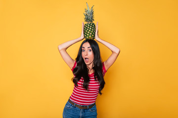 Wall Mural - Pineapple summer party. Beautiful young smiling woman with pineapple in hands on orange background. Tropical fruits. Healthy eating