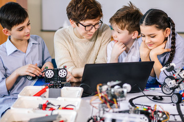 Wall Mural - Team of little curious technicians working together with their teacher in robotics class