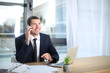 © Africa Studio - Young man in elegant suit talking on cell phone at workplace