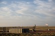 Wide distant view of a completed crude oil well site with a pump jack, natural gas flare, and crude oil production storage tanks in Wyoming, USA