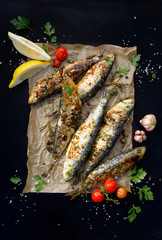 Wall Mural - Grilled sardines on paper and a black background, top view.  Grilled seafood, barbecue